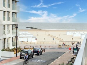A coastal view with a beach, a promenade, and a modern building with balconies. - Apartment in Knoke Near the Beach (Knokke-Heist)