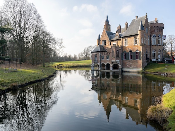 A historic building with a moat, reflecting the structure and surrounding trees.