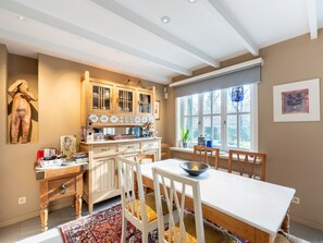 Une cuisine avec des meubles de rangement en bois, une table à manger, des chaises et une grande fenêtre.