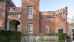 Un edificio de ladrillo histórico con una torre destacada, una entrada en arco y marcos de ventana decorativos.