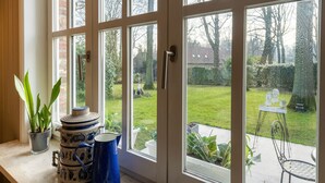 Una habitación con ventanas amplias, una planta en maceta, una jarra azul y un cálido jarrón decorativo sobre una mesa.