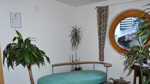 A room with a teal sofa, a potted plant, a small table with a pot, and a window with a curtain. - Retreat in Samnaun Alps (Samnaun)