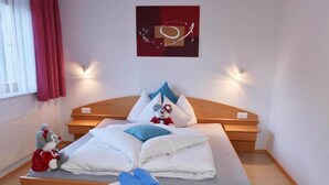 A neatly made bed with pillows and a blanket, a small stool with folded towels, a plush toy on the floor, and a wall-mounted artwork. - Retreat in Samnaun Alps (Samnaun)