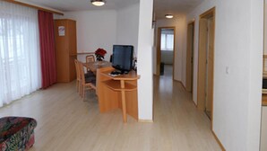 A room with a wooden desk, a television, a dining table with chairs, a sofa, and a hallway leading to another room. - Retreat in Samnaun Alps (Samnaun)