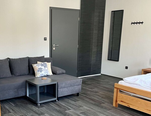 A modern room with a grey sofa, a small side table, a wooden bed, and a dark door. - Village Stay Near Hiking (Horni Marsov)