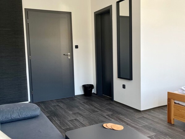 Et moderne værelse med en grå sofa, et lille bord med pude, et trænatbord og et spejl på væggen.