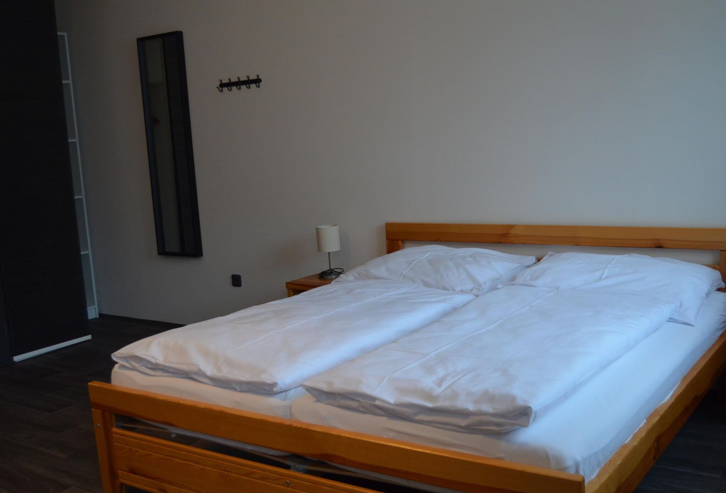 A neatly made bed with white linens in a room with a wooden headboard and a nightstand with a lamp.