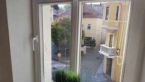 A view through a sliding glass door of a courtyard with a yellow building, a small tree, and a white railing. - Apartment in Kamenz Sachsen Near Town Centre (Kamenz)