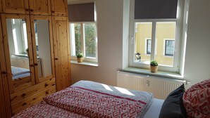 A bedroom with a wooden wardrobe, a bed with patterned bedding, a window with a view of the outside, and a radiator under the window. - Apartment in Kamenz Sachsen Near Town Centre (Kamenz)