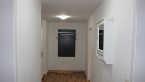 Um corredor estreito com piso de madeira, porta preta e parede branca com uma pequena janela.