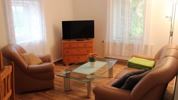 Uma sala de estar com dois sofás de couro, uma mesa de centro de vidro, um armário de madeira com uma TV de tela plana e um abajur.