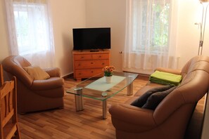 A living room with two leather sofas, a glass coffee table, a wooden cabinet with a flat-screen TV, and a floor lamp. - Ferienwohnung in Struppen (Struppen)