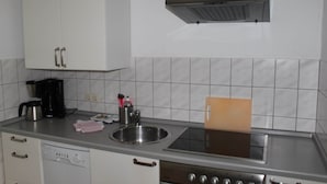 Cozinha com armários brancos, pia de aço inoxidável, cafeteira e micro-ondas.