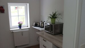 Uma cozinha compacta com janela, torradeira, chaleira e um vaso com planta.