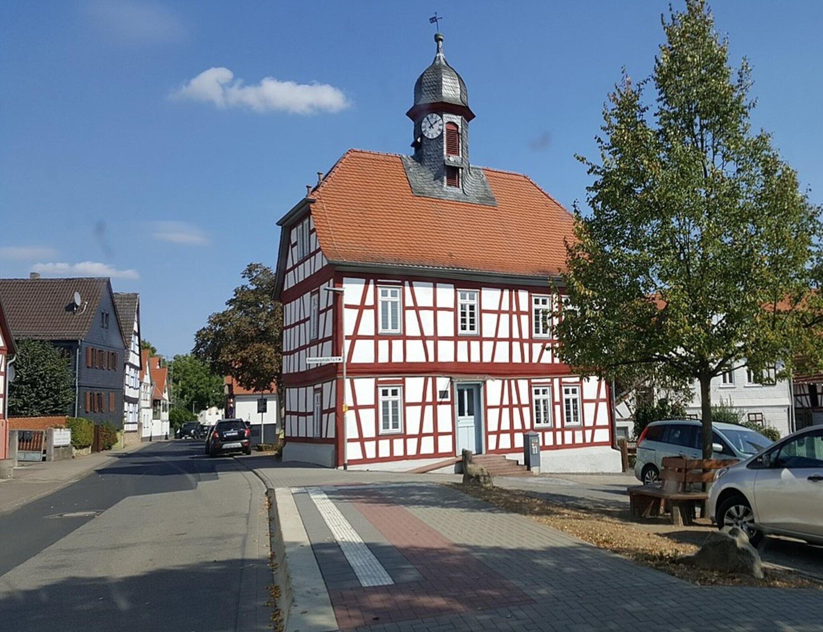 Ein traditionelles Fachwerkhäus mit einem Glockenturm, einer gepflasterten Straße und geparkten Autos.