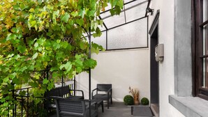 An outdoor seating area with two black metal chairs and a small table, surrounded by greenery and a white wall. - Moselle Riverside Escape (Nehren)