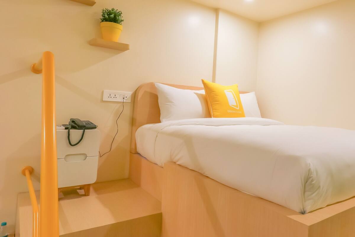 A bedroom with a bed, a nightstand, a phone, a power outlet, and a small potted plant on a shelf.