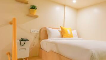 A bedroom with a bed, a nightstand, a phone, a power outlet, and a small potted plant on a shelf.