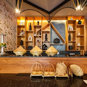 A reception area with a wooden counter, wicker baskets, and shelves with various decorative items. - Bloom Hotel - Golf Course Road, Sector 43 (Gurugram)