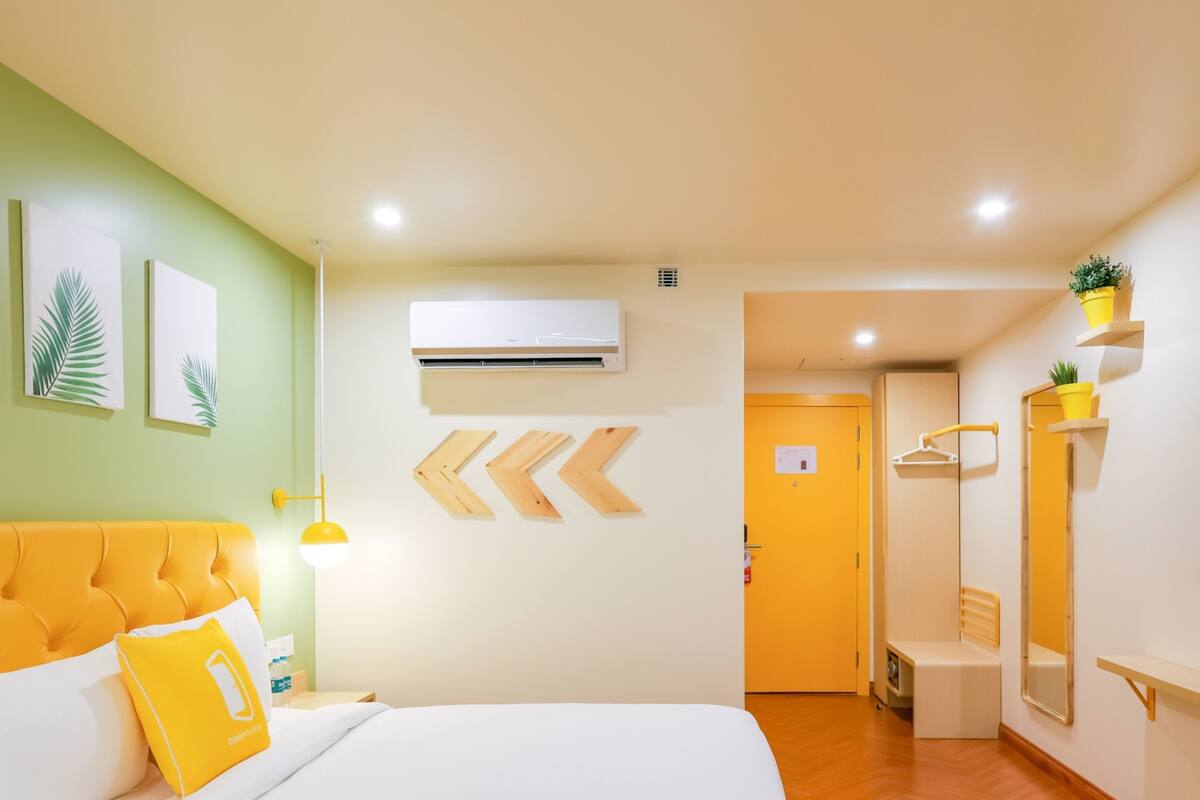 A hotel room with a large bed, a bedside table, a lamp, a mirror, and a door leading to a bathroom.