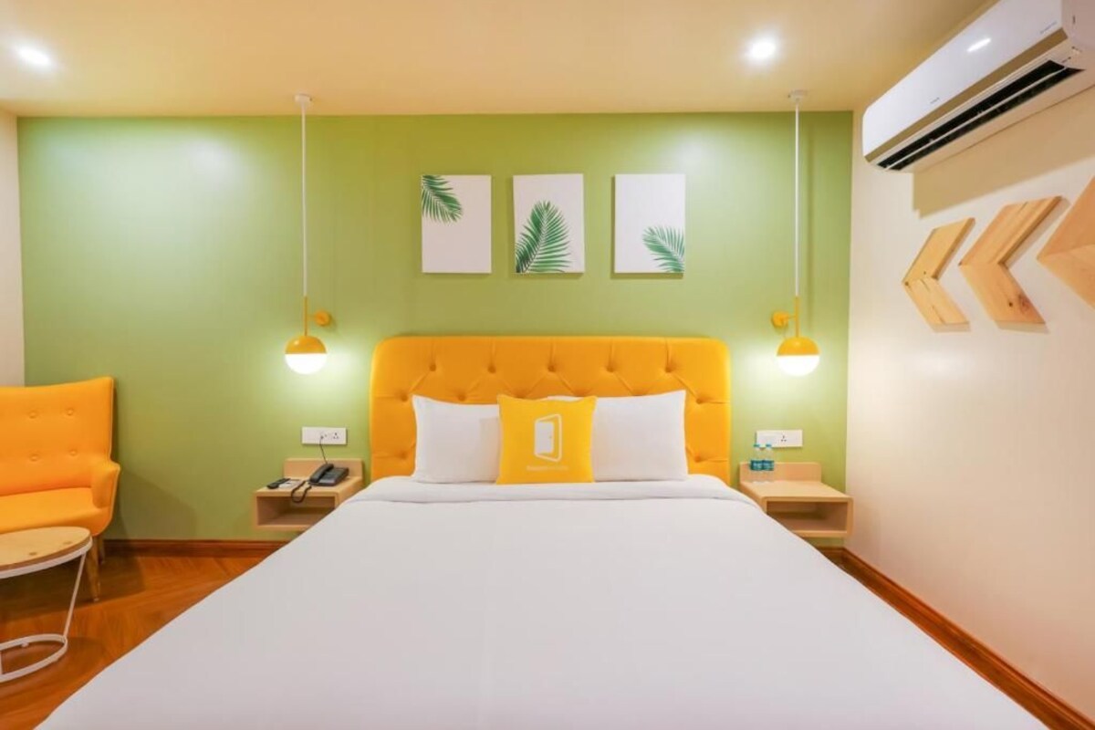 A hotel room with a large bed, a yellow headboard, a green wall, and a wooden floor.