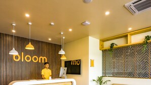 A reception area with a wooden reception desk, a sofa, and a patterned wall. - Bloom Hotel - Golf Course Road, Sector 43 (Gurugram)