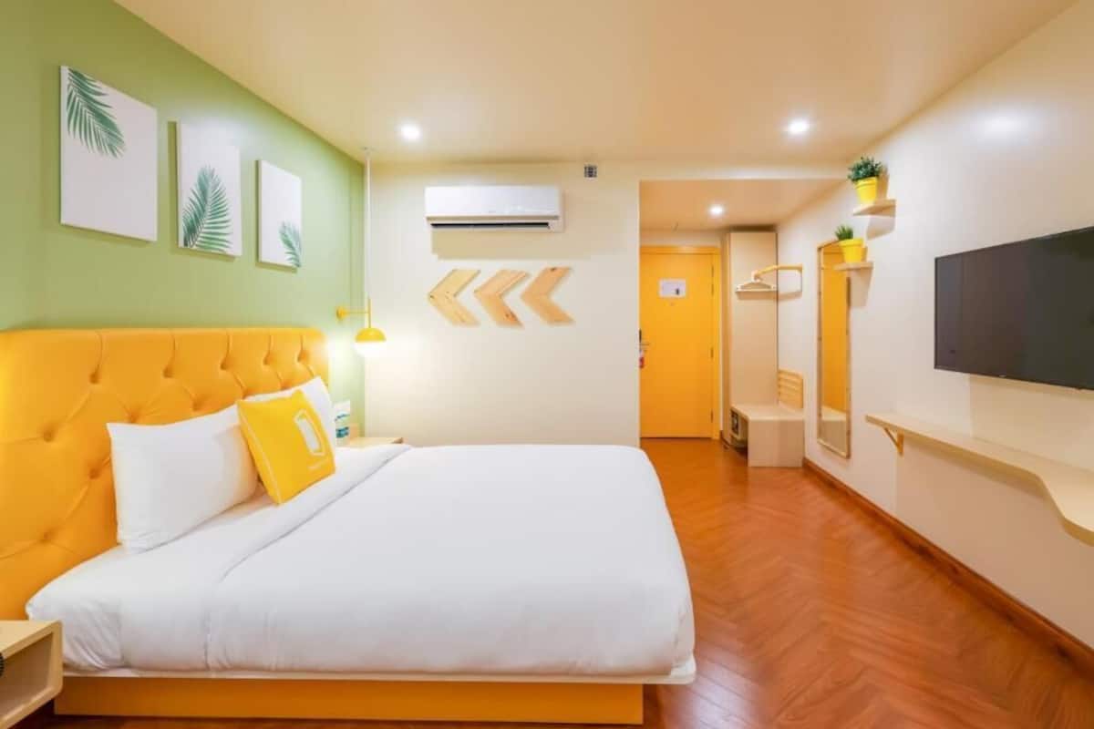 A hotel room with a bed, a nightstand, a TV, and a hallway leading to a bathroom.