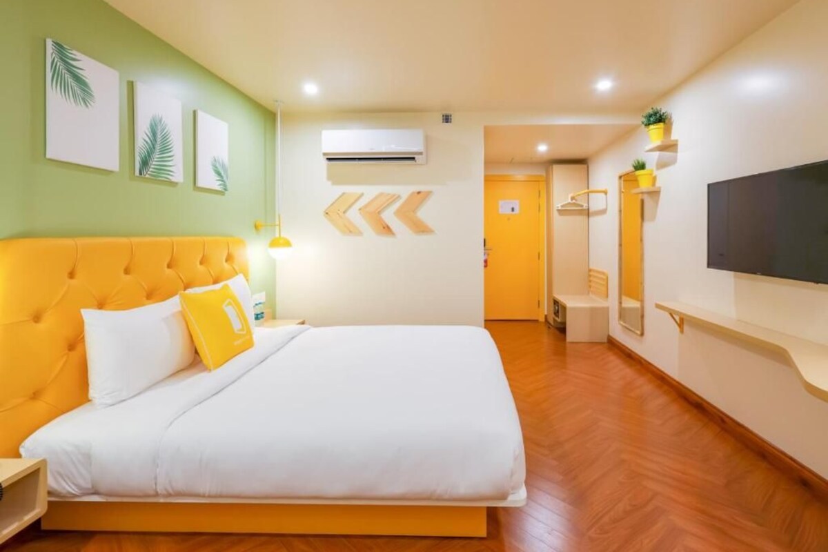 Quarto de hotel com cama, mesa de cabeceira, televisão e corredor que dá para um banheiro.