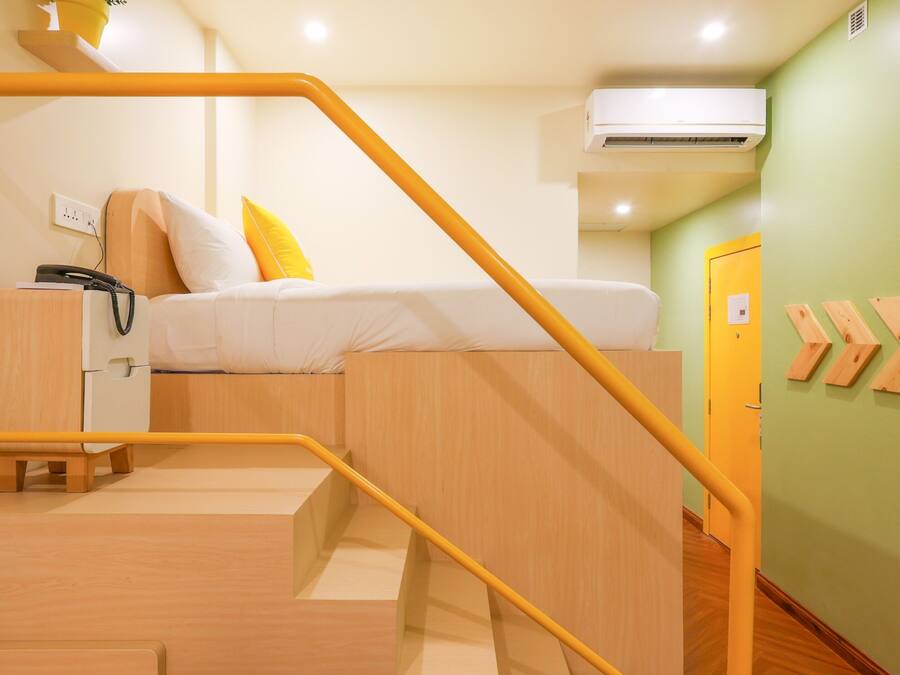 A compact room with a bed, a desk, a chair, and a small staircase with a railing.