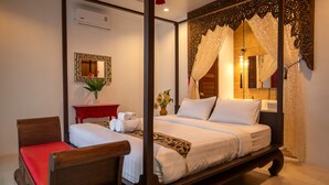 A four-poster bed with white linens, a red chair, a small red table with a vase of flowers, and a mirror on the wall. - Oriental 3br Pool Villa (Rawai)