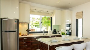 A modern kitchen with a central island, stainless steel appliances, and a view of greenery outside. - Oriental 3br Pool Villa (Rawai)