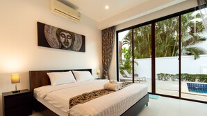 A modern bedroom with a large bed, a nightstand, a wall-mounted air conditioner, and a view of a swimming pool and greenery outside. - Oriental 3br Pool Villa (Rawai)