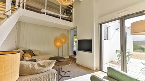 A modern living room with a sofa, two small tables, a TV, and a staircase leading to an upper level. - Noirmoutier-le vieil Charming house with enclosed garden 300m from the beach (Noirmoutier-en-l'Île)