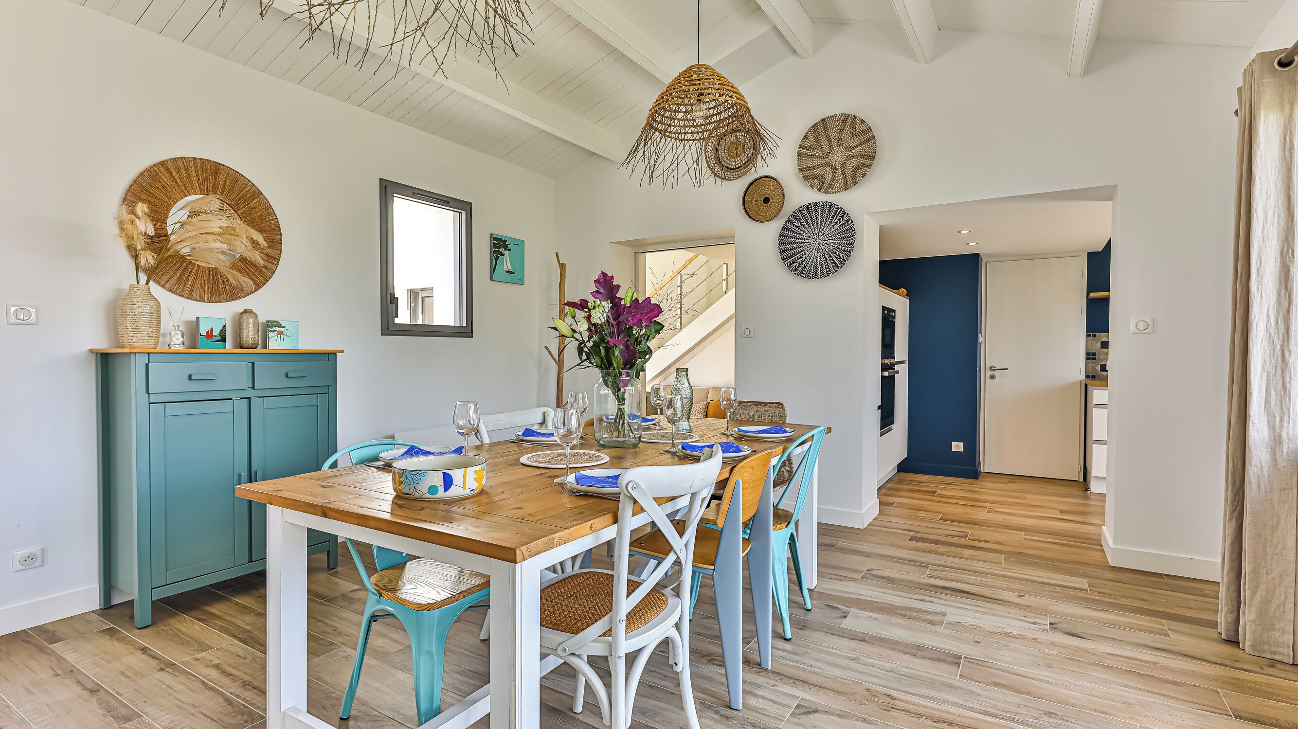 Een eetruimte met een houten tafel voor zes personen, teal stoelen en een teal kast.