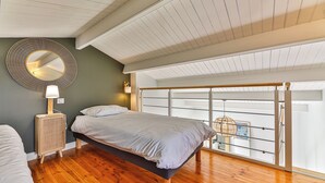 A bedroom with a bed, a round mirror, a bedside lamp, a wooden floor, and a view of the outside through a window with a metal railing. - Noirmoutier-le vieil Charming house with enclosed garden 300m from the beach (Noirmoutier-en-l'Île)
