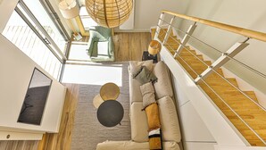 A modern living room with a wooden staircase, a sofa set, and a large window. - Noirmoutier-le vieil Charming house with enclosed garden 300m from the beach (Noirmoutier-en-l'Île)