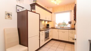 Een kleine keuken met een fornuis, oven en koffiezetapparaat. Er is een raam met uitzicht op groen.