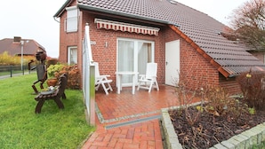 Een huis met een bakstenen gevel, een pannendak en een klein terras met een witte tafel en stoelen.