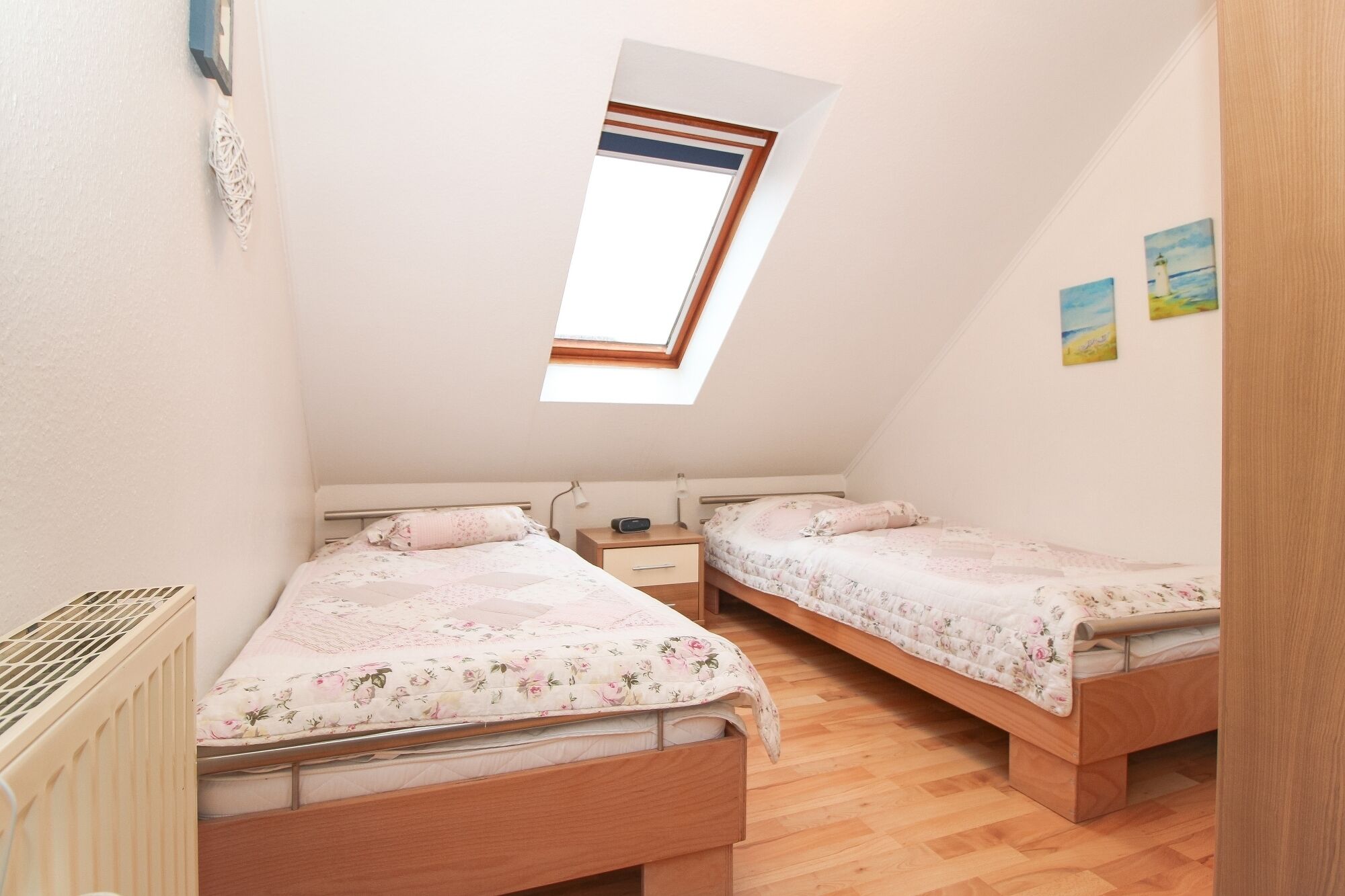 Una habitación pequeña y bien iluminada con dos camas de madera, un tragaluz y un radiador.