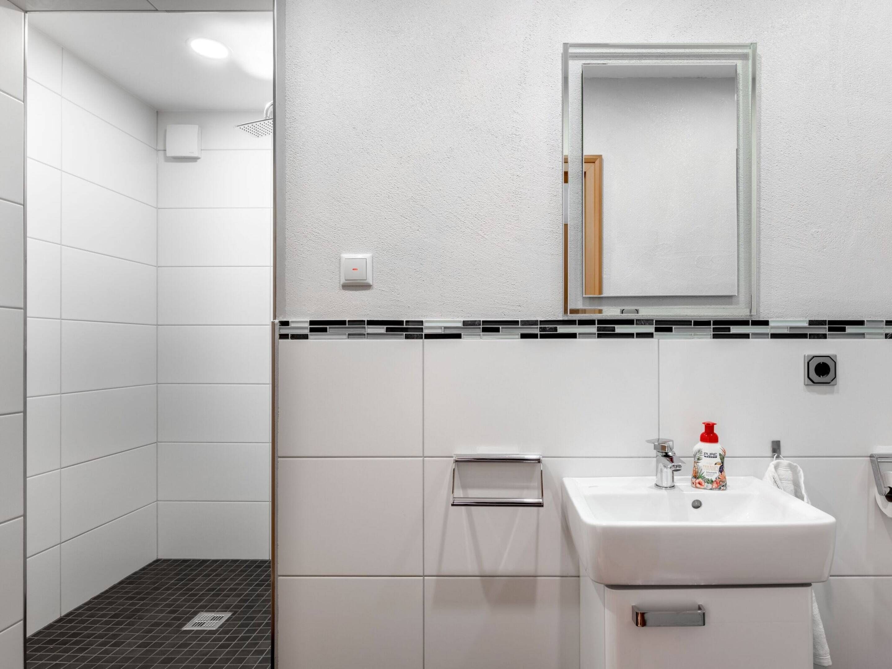 Un baño moderno con azulejos blancos, un lavabo, un espejo y una ducha.