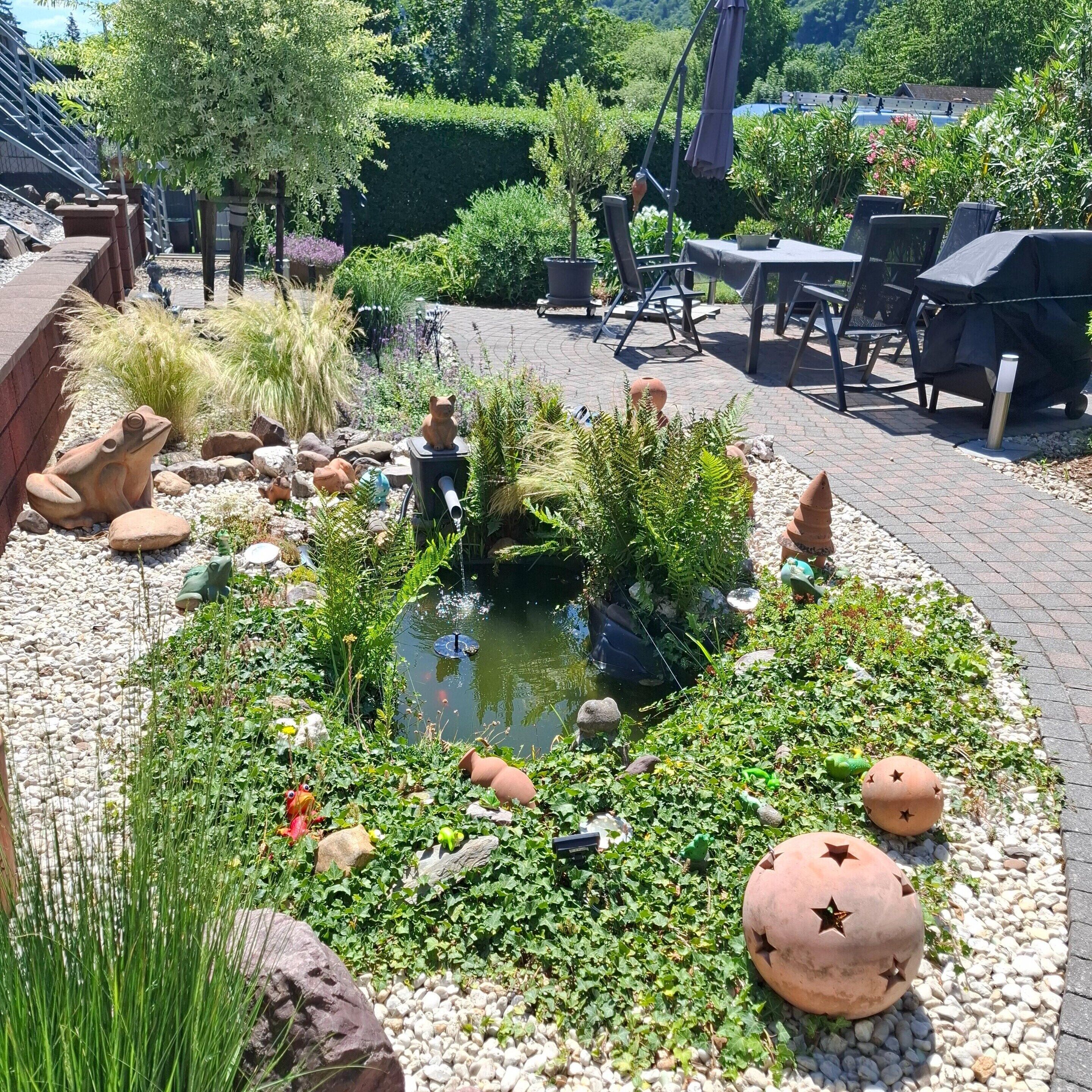 Un jardín con un estanque, macetas decorativas y mobiliario exterior.