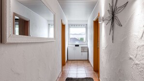 A hallway with white walls, a black rug, a decorative wall piece, and a window with a view of the outside. - Garden Retreat With Pond View (Neumagen-Dhron)