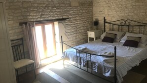 Une chambre avec un mur en pierre, un lit avec une literie blanche, une table de chevet et une chaise.
