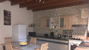 Une cuisine compacte avec un mur en pierre, des armoires en bois, un réfrigérateur blanc et un coin repas comprenant une table et des chaises.