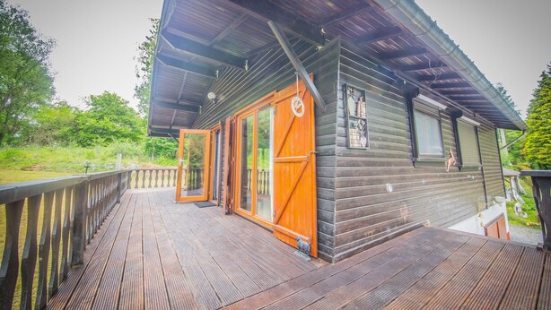 A wooden cabin with a deck, large windows, and a covered porch. - Chalet in Rendeux With Garden (Rendeux)