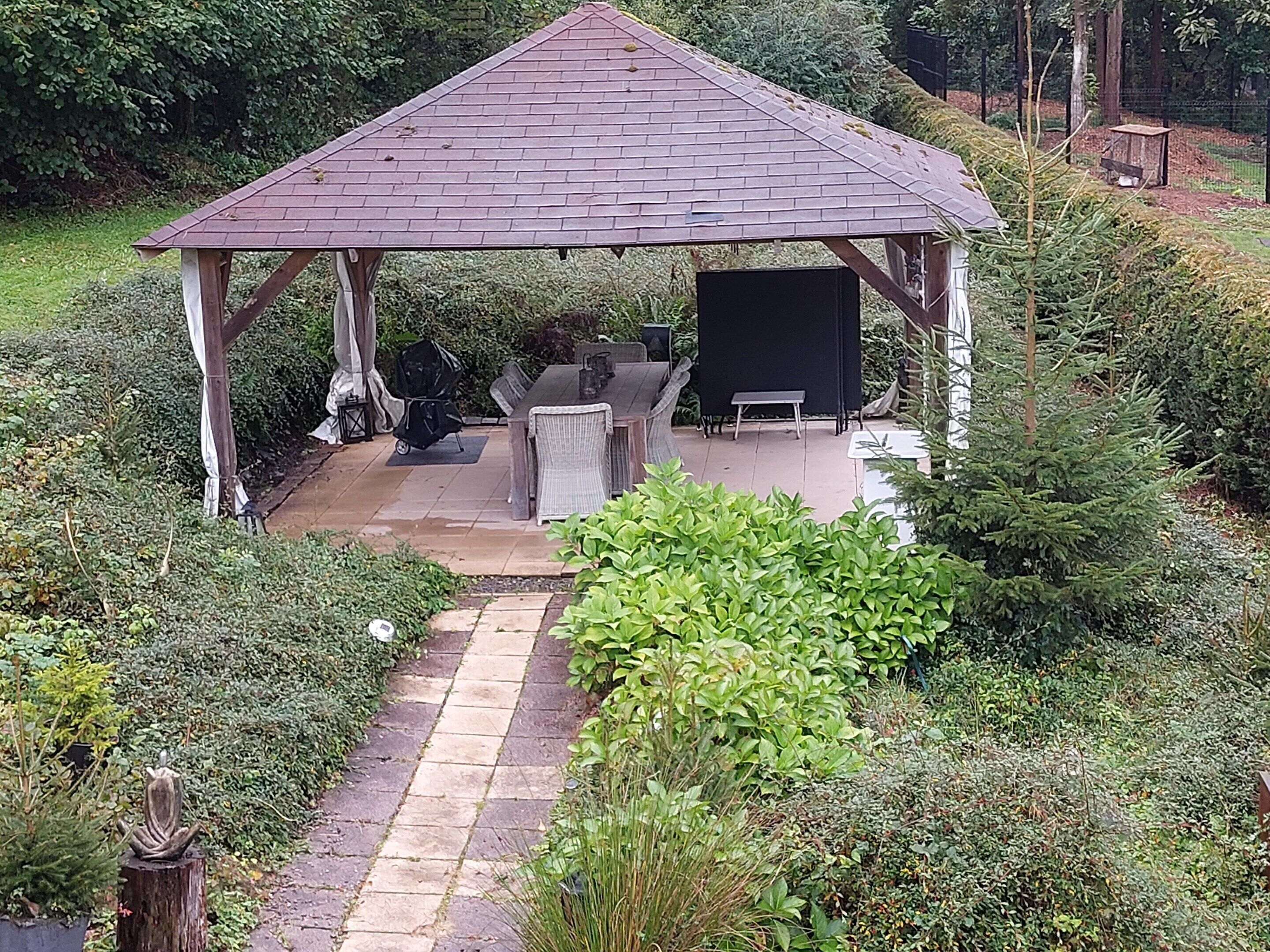 A gazebo with a tiled roof, surrounded by lush greenery and a stone pathway leading to it.