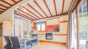 A modern kitchen with wooden beams, a dining area with a glass table, and a view of the outdoors. - Chalet in Rendeux With Garden (Rendeux)