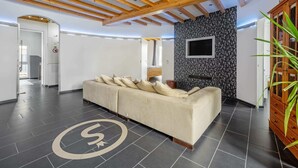 A modern hotel lobby with a sofa, wooden ceiling beams, a TV mounted on a black floral wall, and a plant. - Co2-neutrale und Barrierefreie Ferienwohnung im Sauerland (Herscheid)