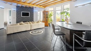 A modern living room with a sofa, a dining area with a table and chairs, a TV mounted on a wall, and a wooden ceiling structure. - Co2-neutrale und Barrierefreie Ferienwohnung im Sauerland (Herscheid)