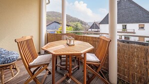 A wooden table and chairs on a balcony with a view of houses and mountains. - Co2-neutrale und Barrierefreie Ferienwohnung im Sauerland (Herscheid)